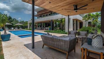 A modern outdoor living area with a pool, lounge chairs, and a ceiling fan.
