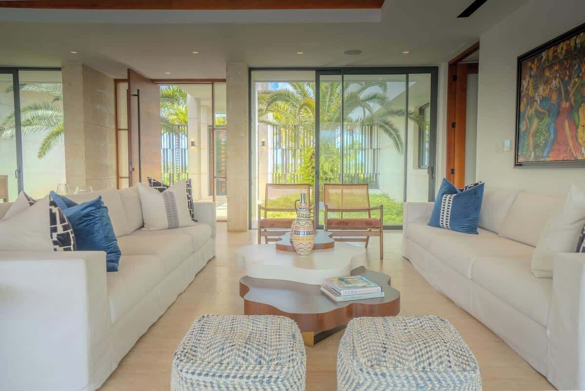 A modern living room with a sofa set, a coffee table, and a view of palm trees through large windows.