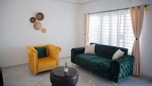 A living room with a yellow armchair, a green sofa, a round black side table, and a window with curtains.