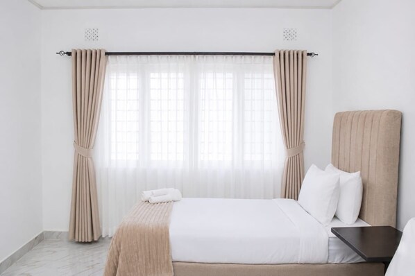 A hotel room with a bed, a bedside table, and curtains.