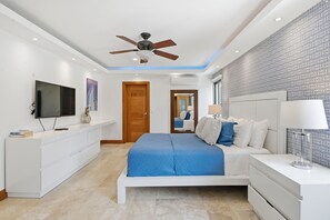 A modern bedroom with a bed, bedside table, TV, and a ceiling fan.