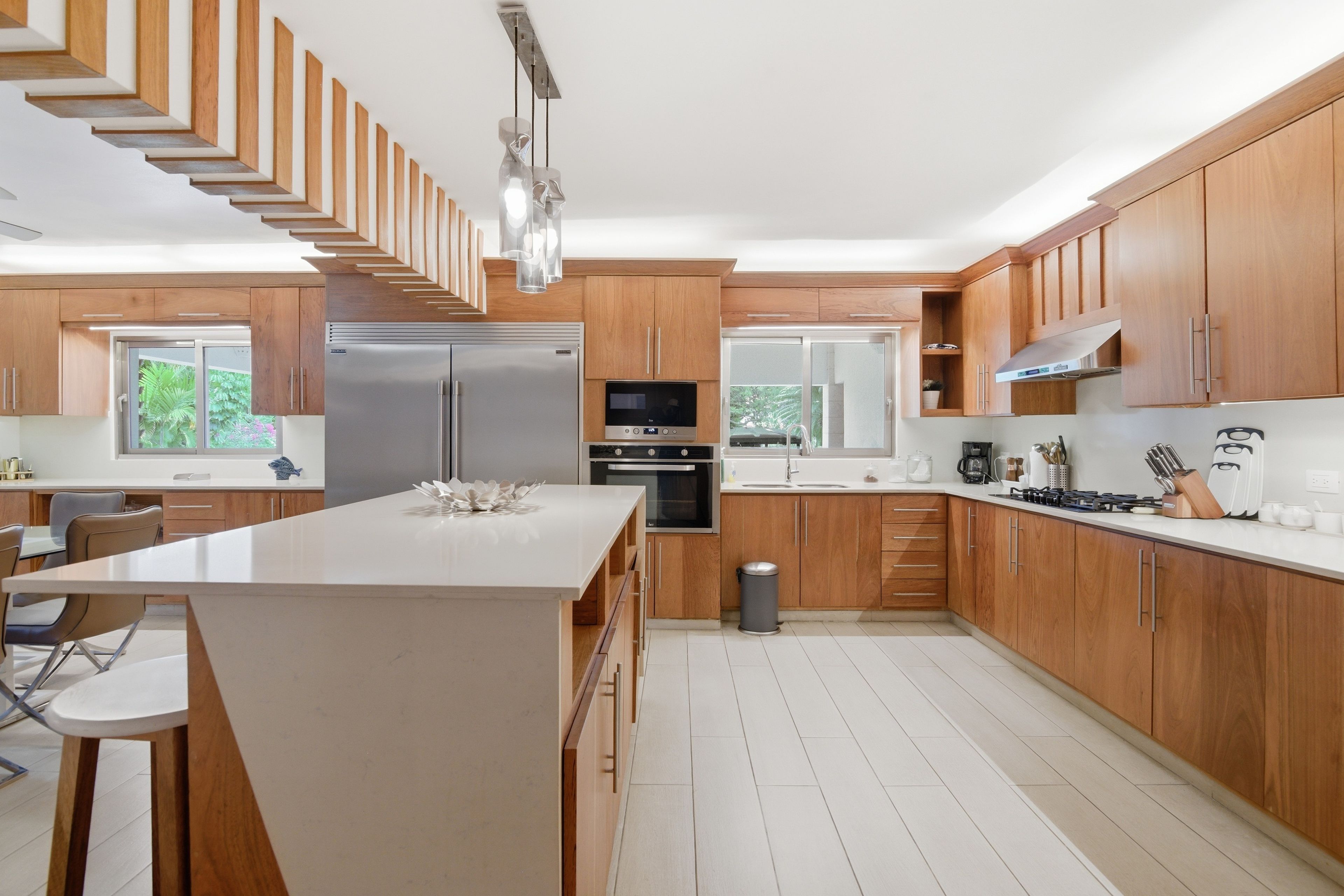A modern kitchen with wooden cabinetry, a central island, stainless steel appliances, and a view of greenery outside.