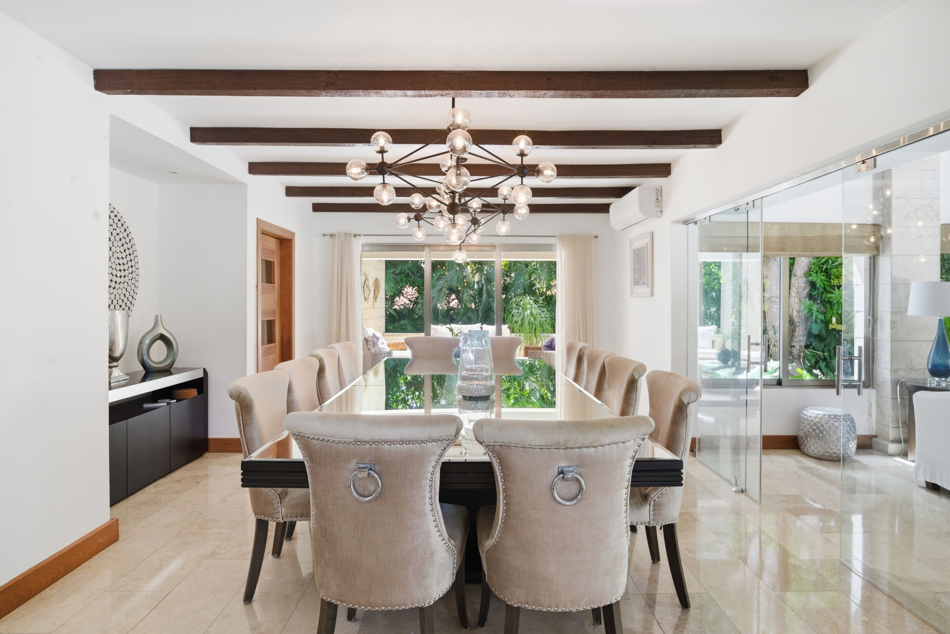 A dining area with a modern chandelier, a glass-top table, and upholstered chairs.