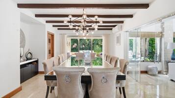 A dining area with a modern chandelier, a glass-top table, and upholstered chairs.