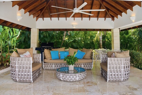 An outdoor patio with a ceiling fan, a round glass table, and wicker furniture.