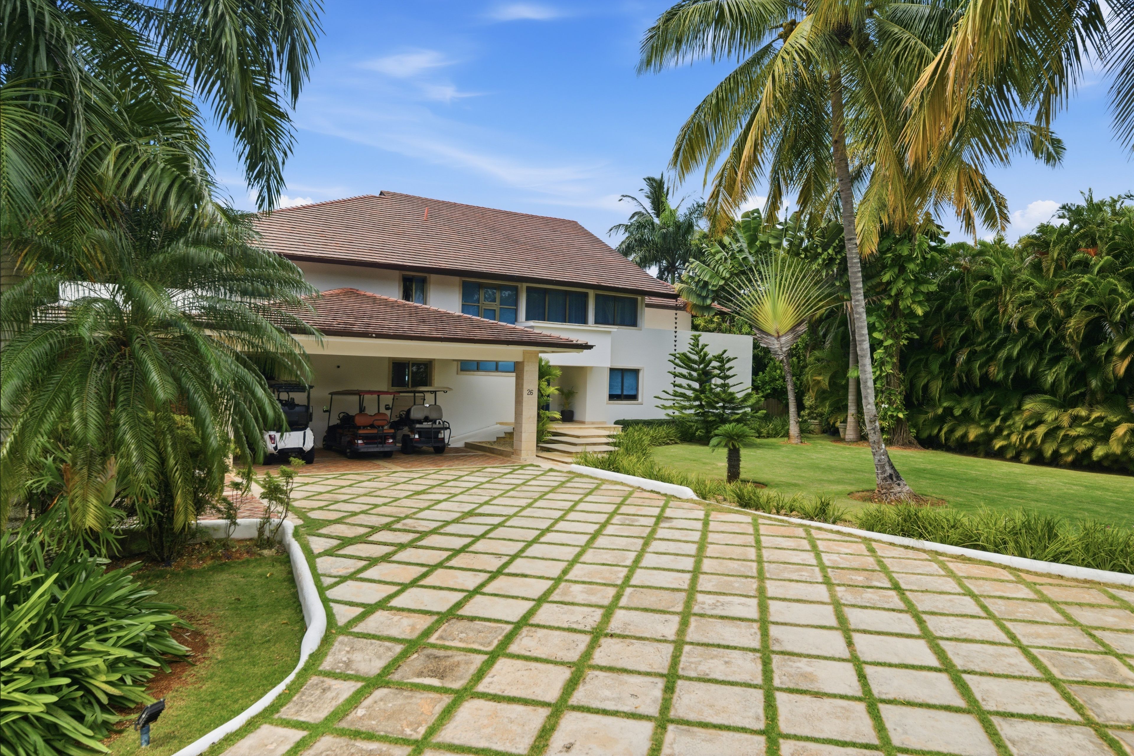 A two-story house with a tiled roof, a covered driveway, and a well-maintained lawn.