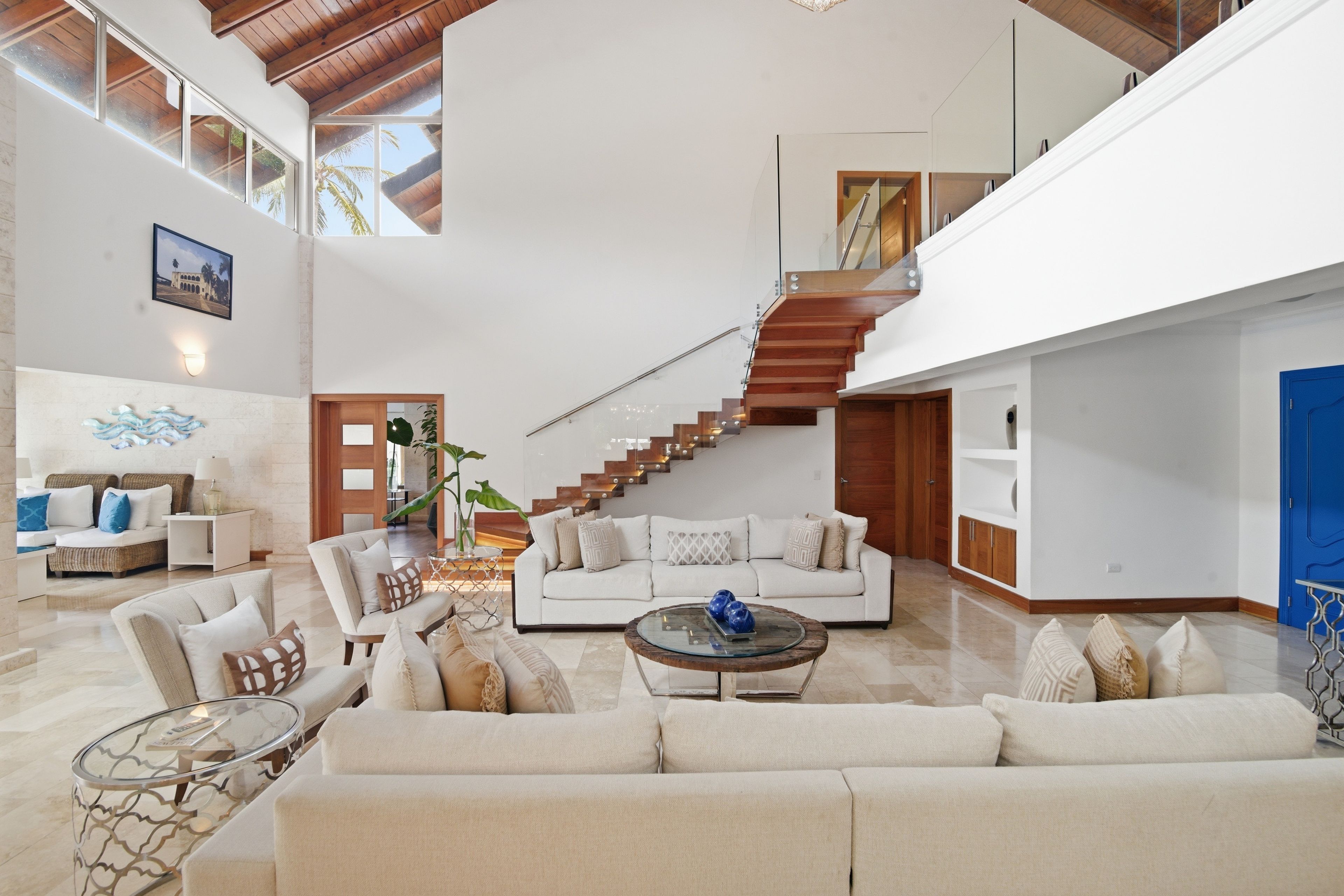 A spacious living area with a high ceiling, a staircase, and a large window.