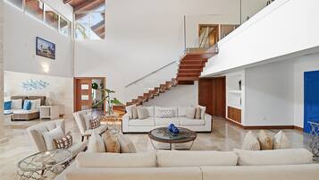 A spacious living area with a high ceiling, a staircase, and a large window.