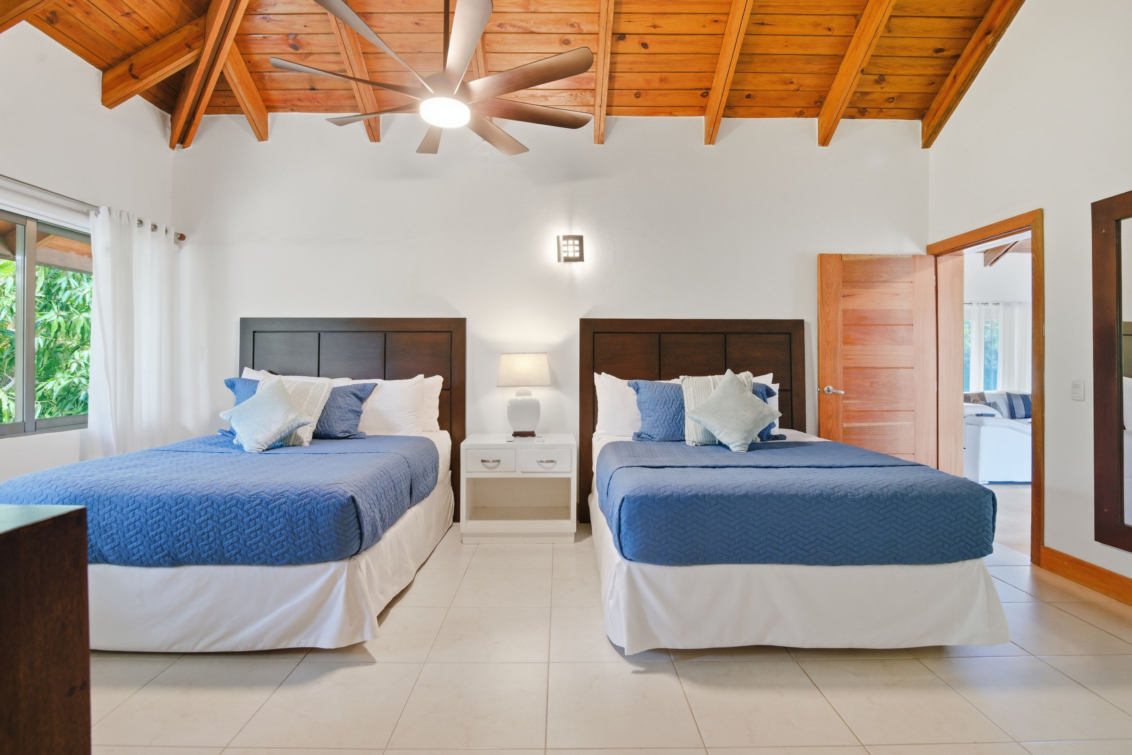 A hotel room with two beds, a ceiling fan, a nightstand, and a window with curtains.