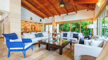 A spacious living area with a high ceiling, a central coffee table, and a seating arrangement including a blue chair and white sofas.
