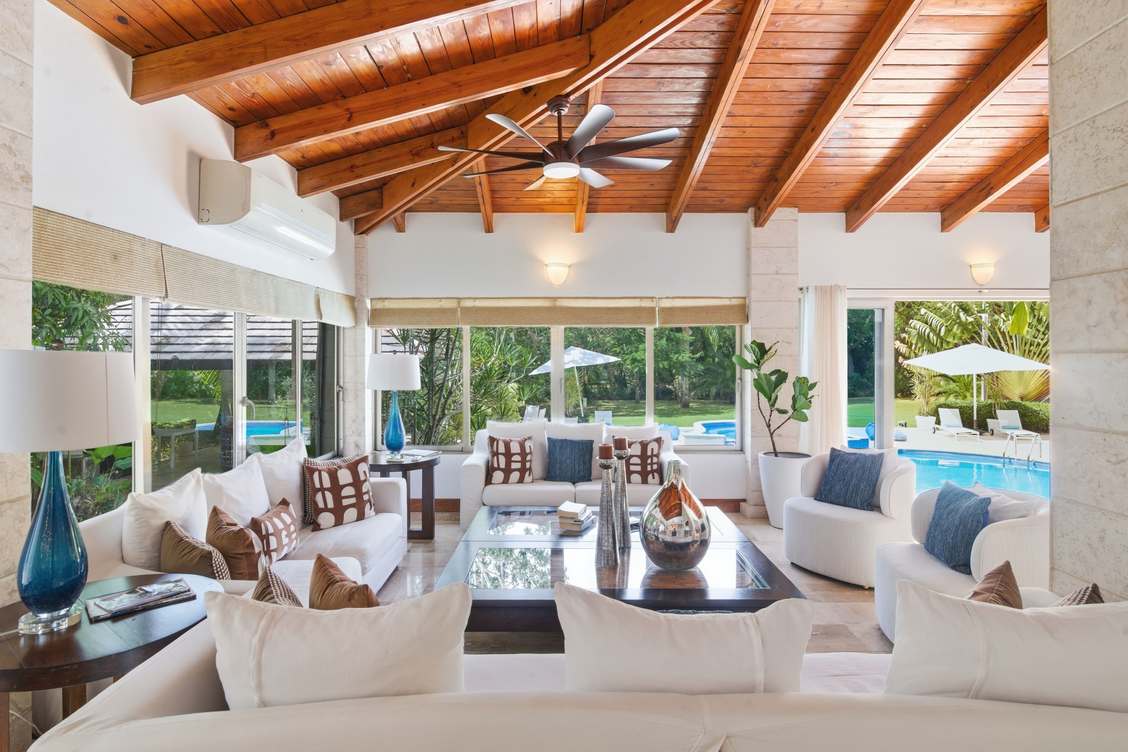 A spacious living area with a ceiling fan, large windows, and a view of a swimming pool.