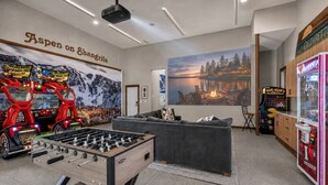 Een kamer met een tafelvoetbaltafel, een bank, een muur met een landschapschilderij en een grijpmachine.