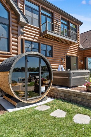 A log cabin with a large circular window, a hot tub, and a balcony overlooking a body of water.