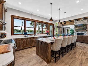 A spacious kitchen with a large island, wooden cabinetry, and a view of a tropical landscape.