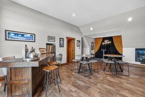 A modern kitchen with a bar area, wooden flooring, and a dining space with stools.