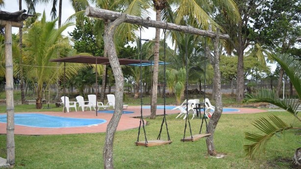Um parquinho com balanços, uma piscina pequena e cadeiras de plástico branco.