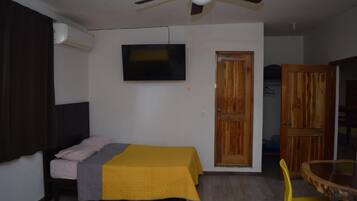 Un dormitorio con una cama, ventilador de techo, televisor y puerta de madera.