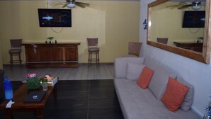 Sala de estar com sofá, cadeiras, mesa de centro, televisão e um espaço de bar.