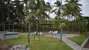 Área de piscina com balanços, palmeiras e uma estrutura de concreto.