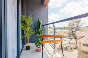 A balcony with potted plants, a wooden bench, and a view of a residential area. - Cosy and well decorated apartment in Riara one residency.cool and friendly! (Nairobi)