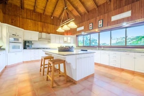 Una cucina con mobili bianchi, una grande isola con sgabelli, un forno integrato e una finestra con vista sugli alberi.