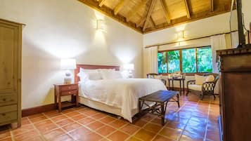 A bedroom with a bed, bedside tables, a chair, a desk, and a window with a view of greenery.