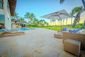 A poolside area with lounge chairs, a covered seating area, and a view of palm trees. - Villa Vega de Palma. Luxurious villa .Golf view (La Romana)