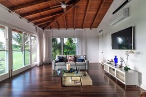 A spacious living room with a wooden ceiling, large windows, a grey sofa, a glass coffee table, and a flat-screen TV. - Villa Vega de Palma. Luxurious villa .Golf view (La Romana)