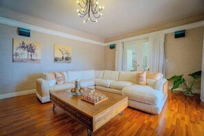 Ein Wohnzimmer mit einem Ecksofa, einem Couchtisch aus Holz mit einem Schachspiel und zwei an der Wand befestigten Kunstwerken.