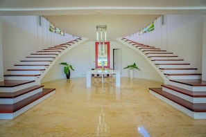 Un intérieur spacieux avec un escalier central, flanqué de deux murs, un plancher poli et une table au centre.