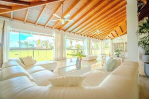 A spacious living area with a high ceiling and wooden beams, large windows, and a view of a green landscape. - Villa Vega de Palma. Luxurious villa .Golf view (La Romana)