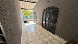 A covered outdoor area with tiled flooring, a bench, and a metal gate leading to a fenced garden.