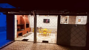 A kitchen with a brick oven, a dining area with yellow chairs, and a tiled wall with a television.