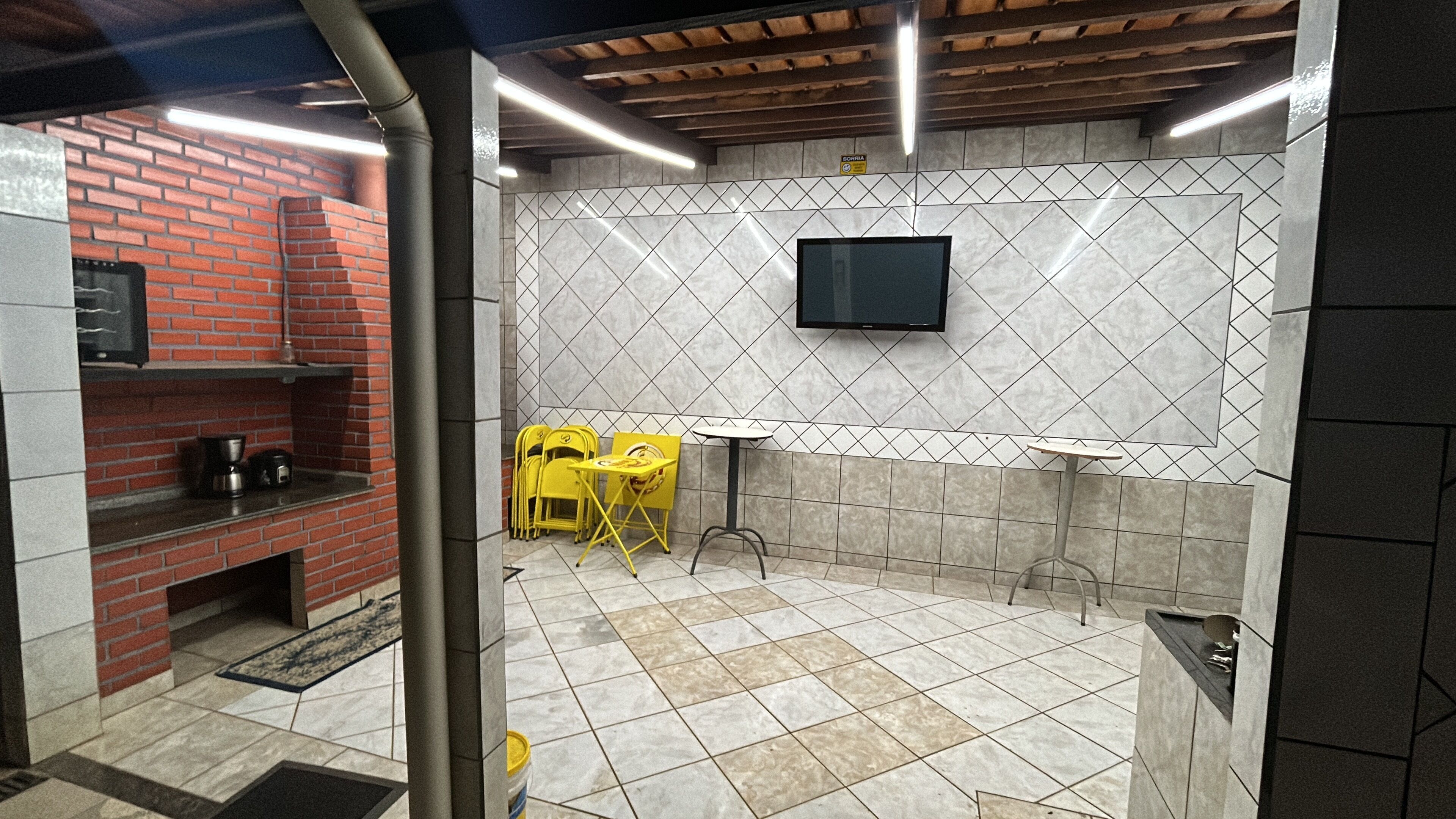 A modern kitchen with a brick wall, tiled backsplash, and a flat-screen TV mounted above a countertop.