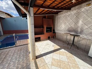 An outdoor patio with a brick fireplace, a pool, and a tiled floor.