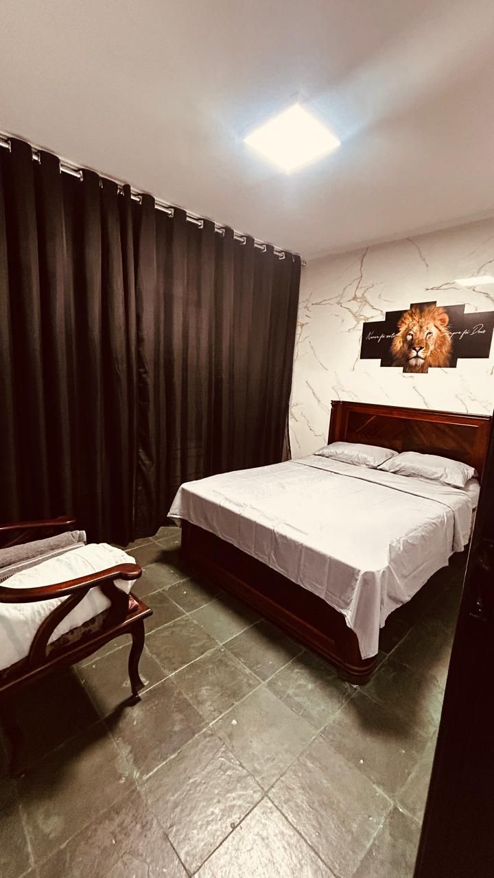 Quarto com cama, uma cadeira, uma obra de arte na parede e iluminação no teto.