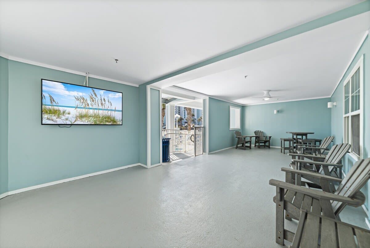A spacious room with a large TV, wooden chairs, and a view of the outdoors.