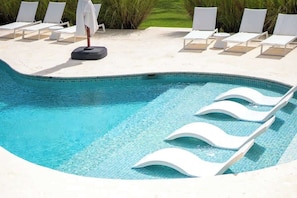 A swimming pool with white lounge chairs and umbrellas.