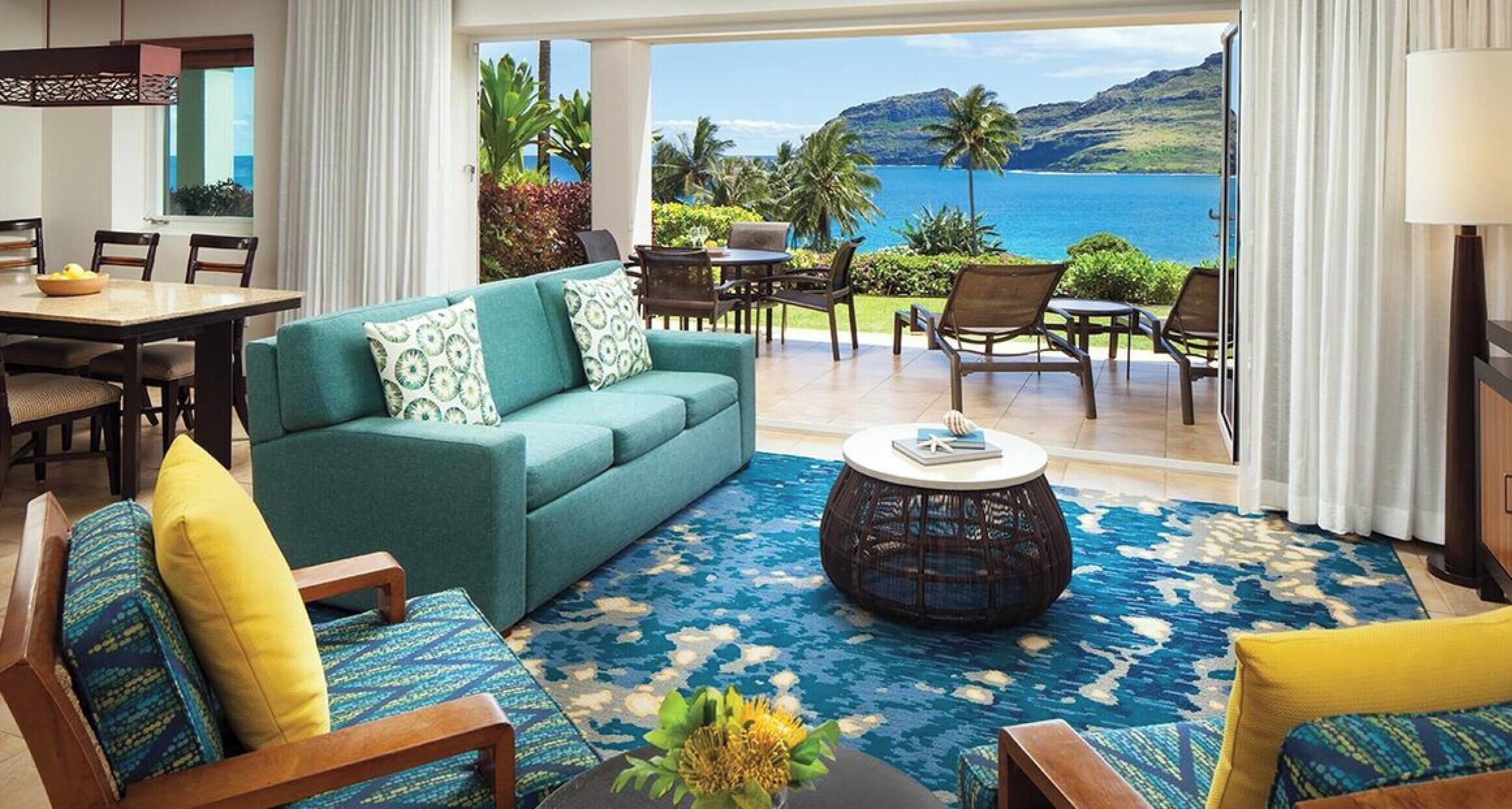 A room with a sofa, chairs, a dining table, and a view of the ocean.