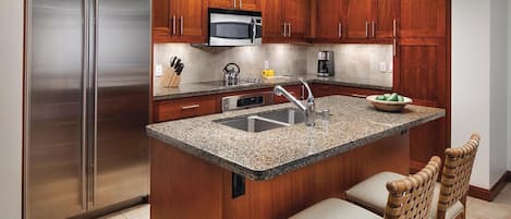 Una cocina con refrigerador de acero inoxidable, microondas, pileta y gabinetes de madera.