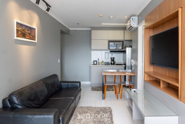 Una sala de estar moderna con un sofá de cuero negro, una mesa de centro de vidrio y un televisor montado en una pared de madera.