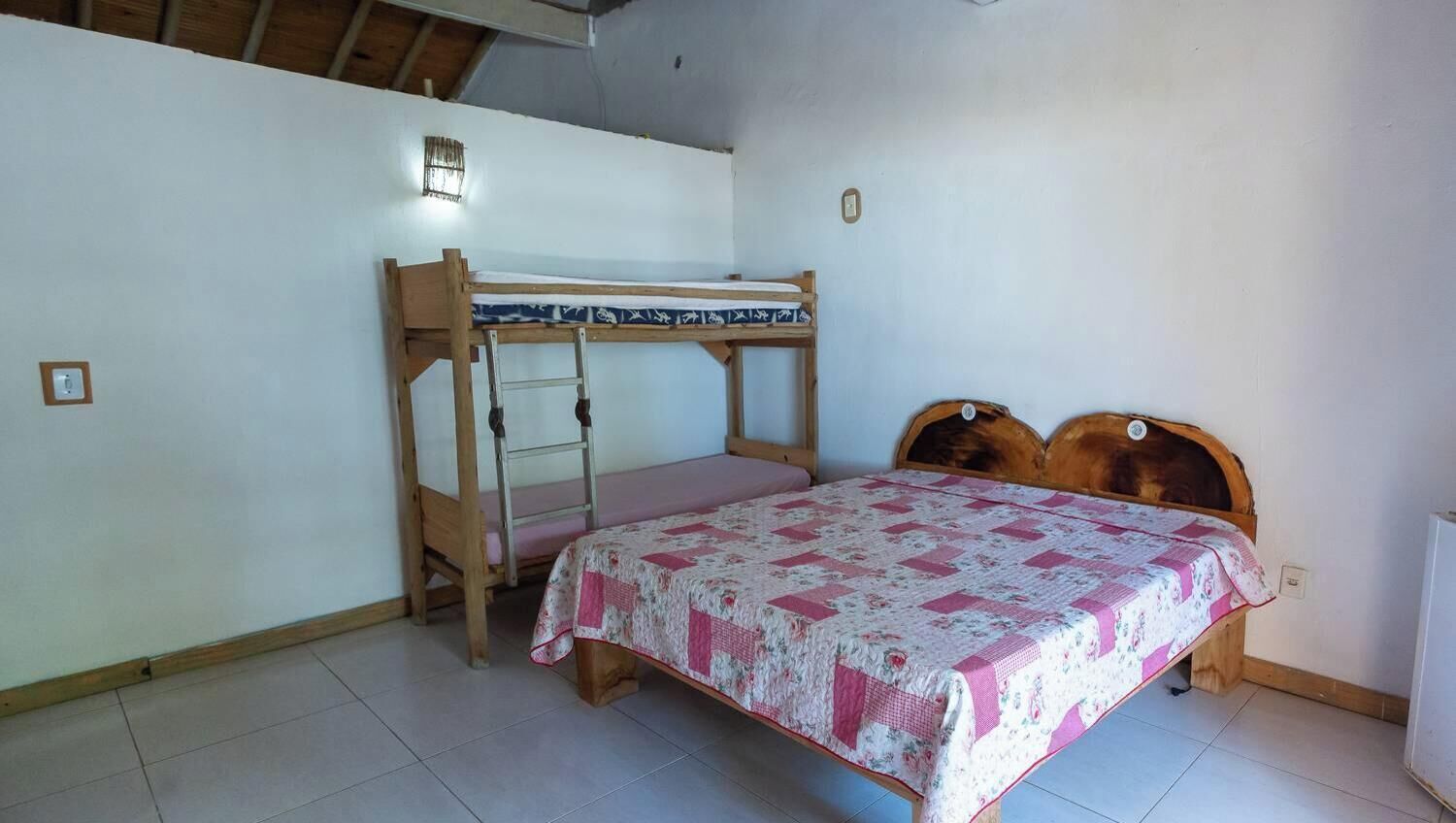 A room with a bunk bed, a single bed, a ladder, and a wall-mounted light fixture.
