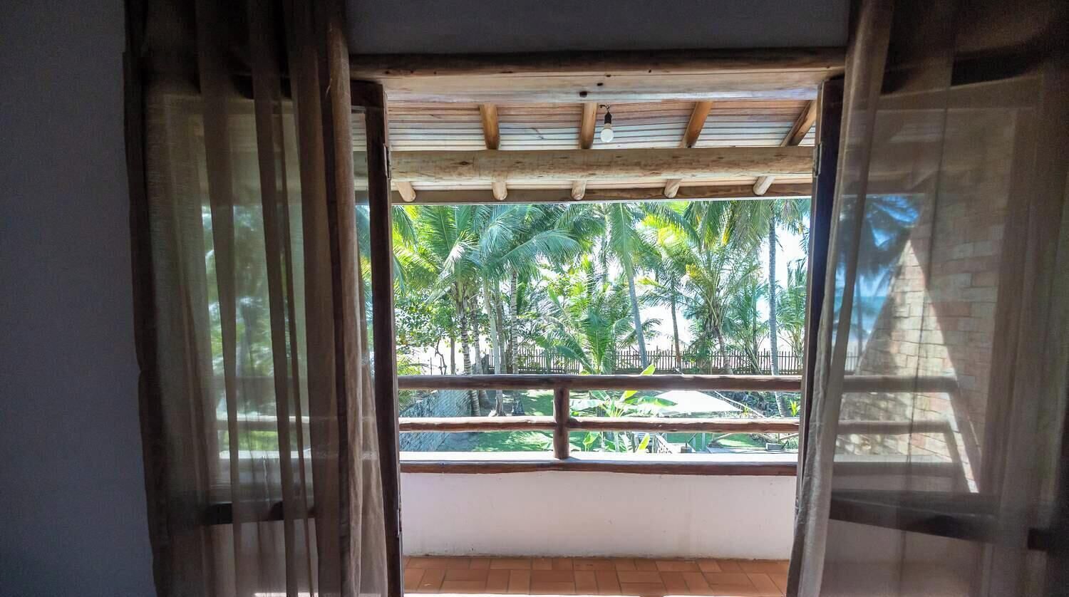 A room with a view of palm trees through a window with a wooden frame and a balcony railing.