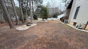 Ein Wohngrundstück mit einer Holzdiele, einem kleinen Gartenhaus und einem Haus mit weißer Fassade.