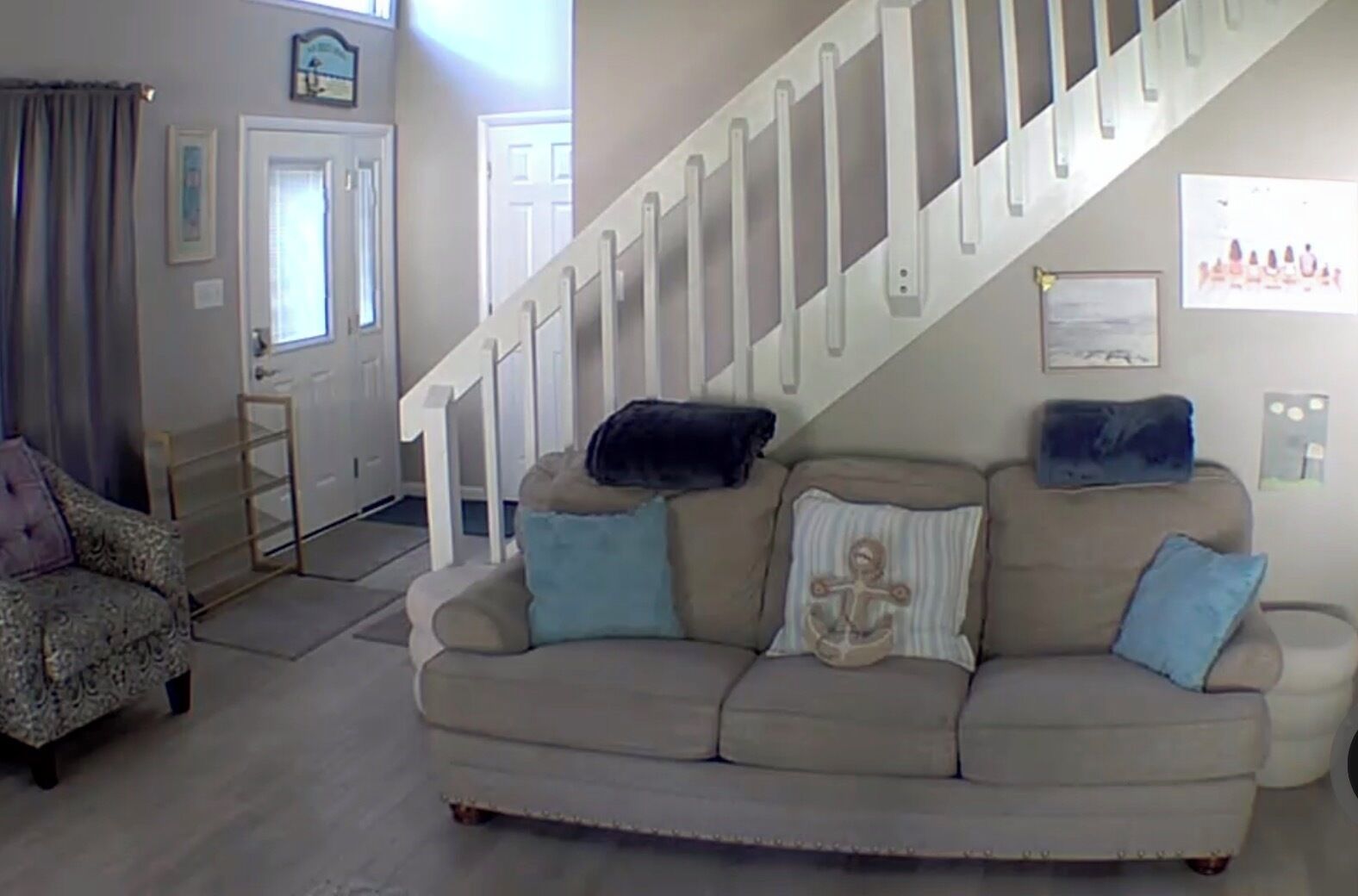 A living room with a beige sofa, a patterned armchair, and a staircase.