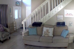 A living room with a beige sofa, a patterned armchair, and a staircase. - Cozy 3-bedroom house in charming Ocean Pines with AC (Ocean Pines)