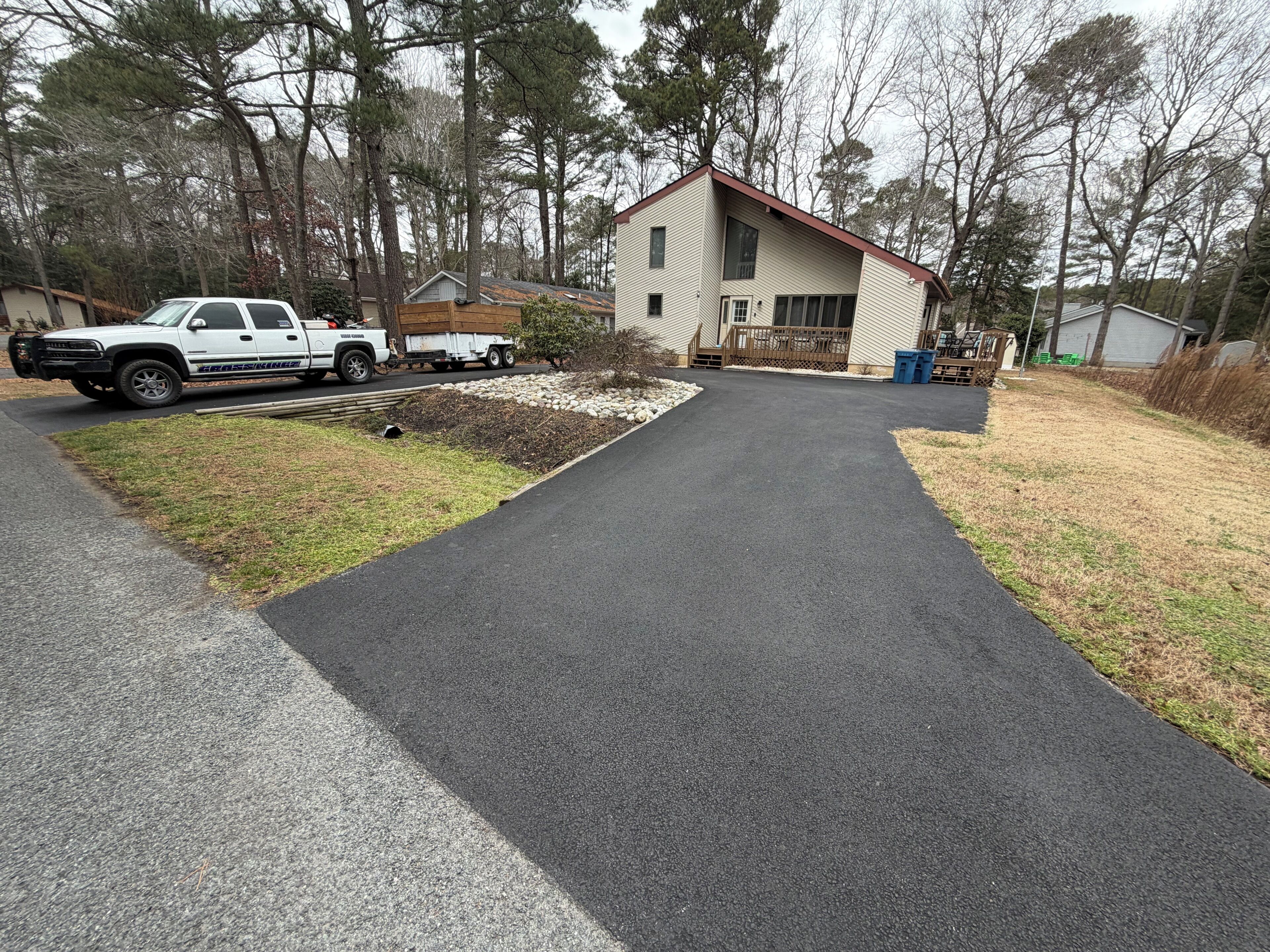 A residential driveway leading to a house with a wooden deck and a garage.