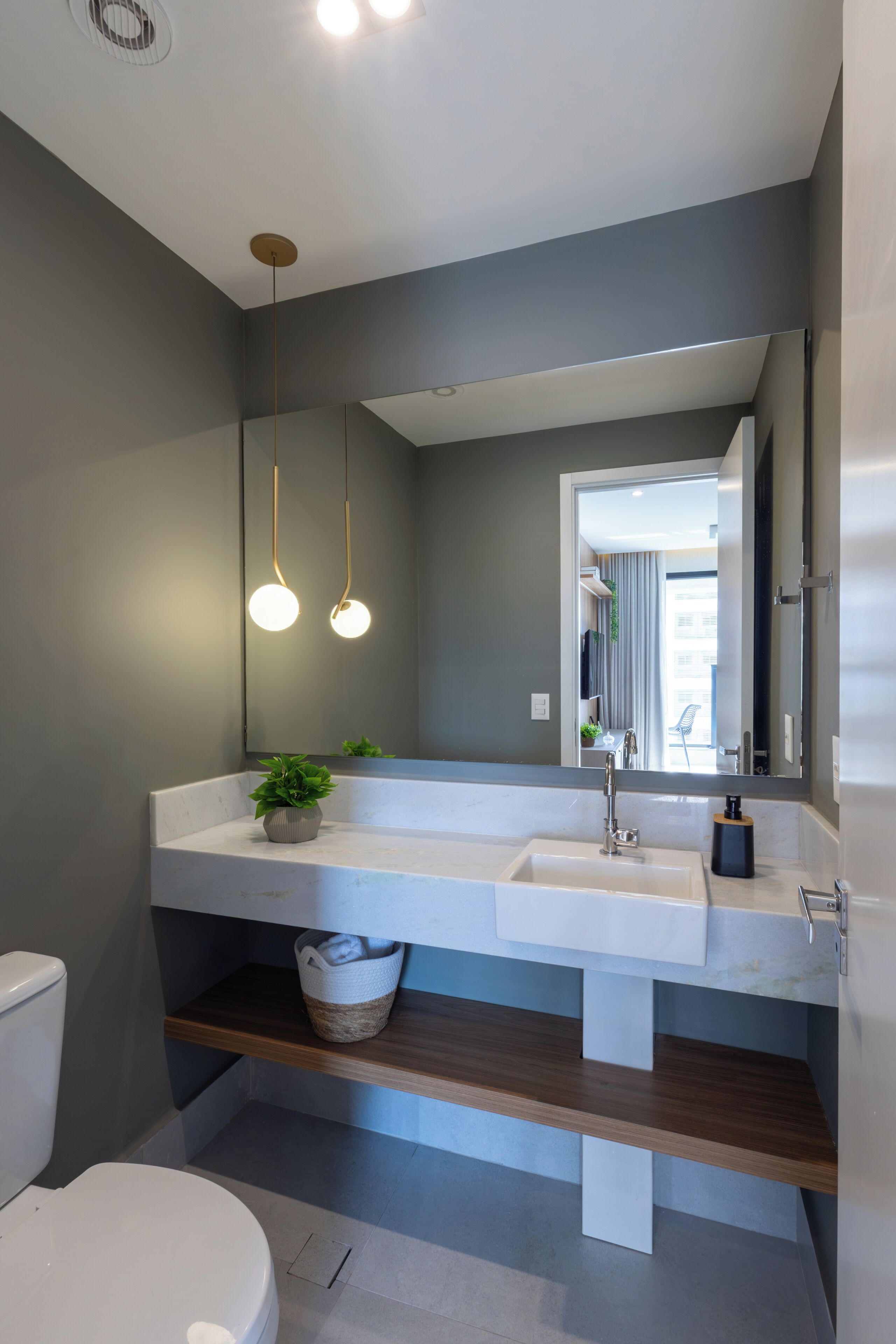 A modern bathroom with a dual sink vanity, a large mirror, a hanging light fixture, and a potted plant.