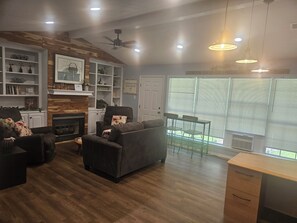 Ein Wohnzimmer mit Kamin, einer Couch, einem Esstisch mit Stühlen und einem Deckenventilator.