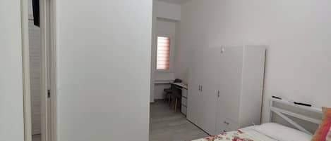 Un dormitorio con cama, armario y escritorio con silla.